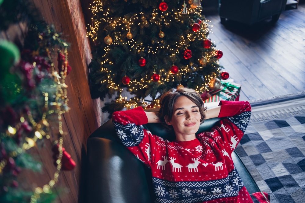 woman in holiday sweater relaxing and practicing self-care on a couch to prevent any holiday triggers 