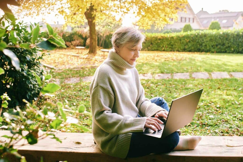 Outdoor portrait of mature 55 - 60 year old woman using laptop in garden