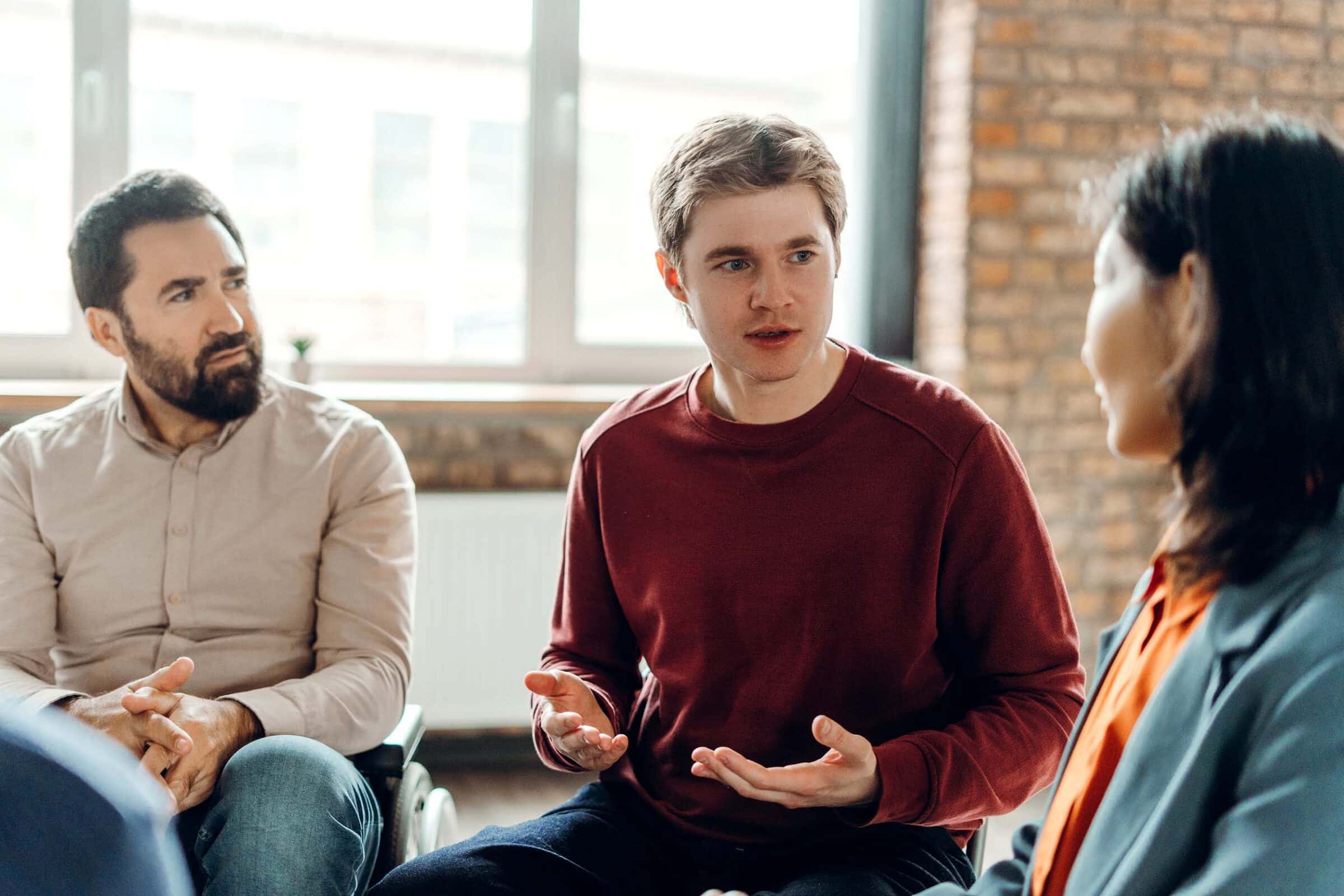 Young man actively participates in a support group, sharing his thoughts and experiences with attentive listeners in a therapeutic setting.