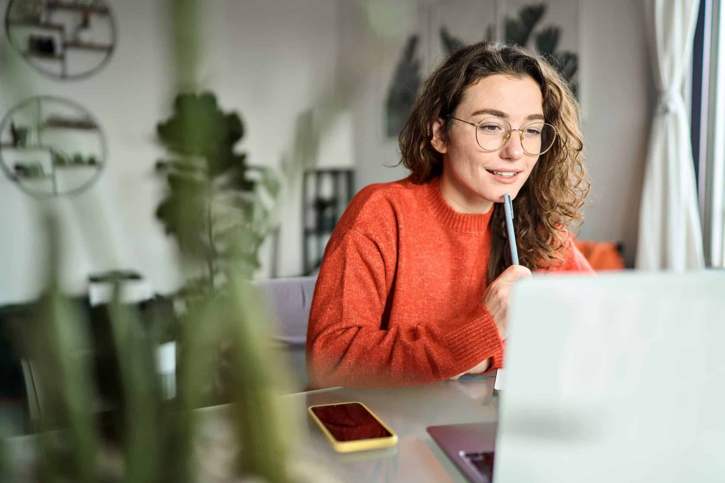 Young woman studying, focused on her laptop in home office.