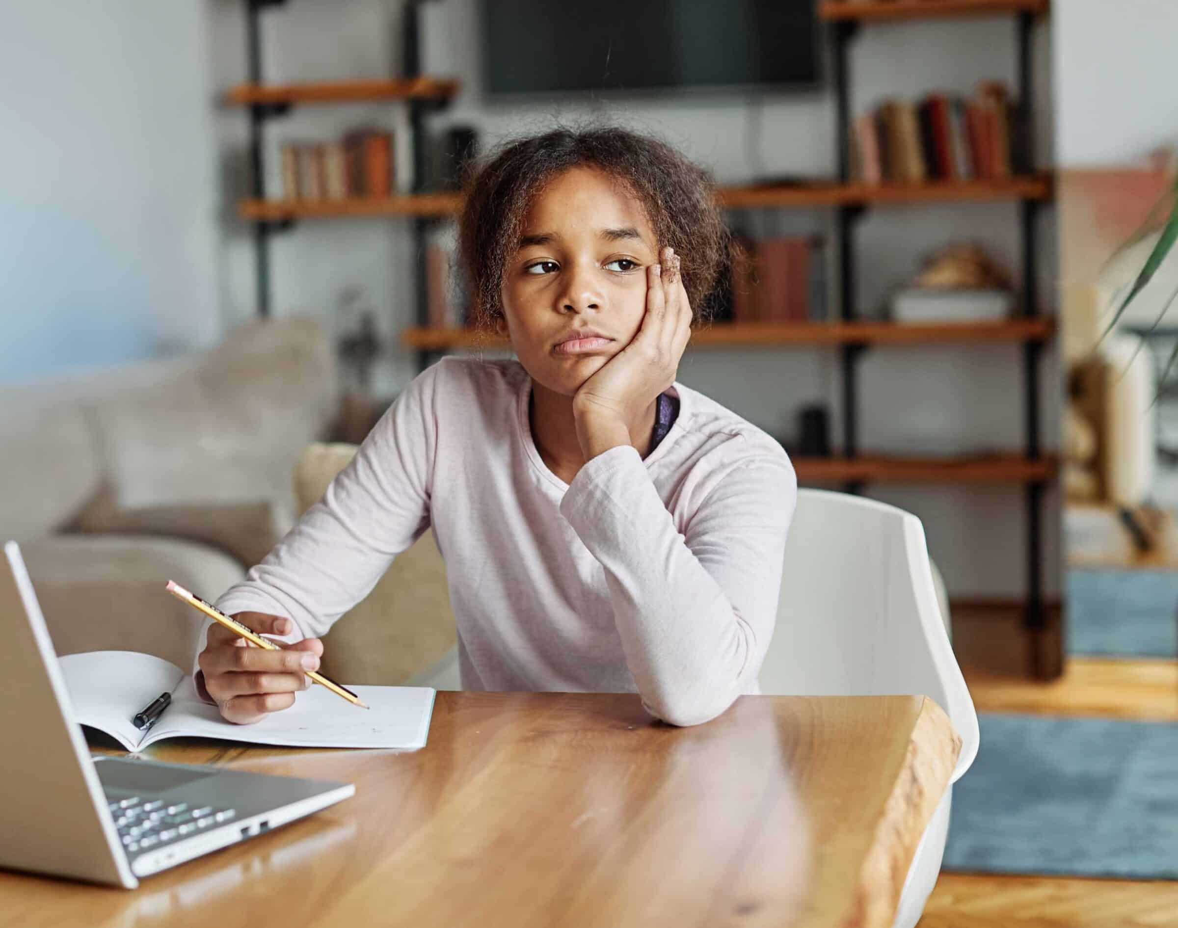 Young girl sitting bored while studying with an open laptop in dining room