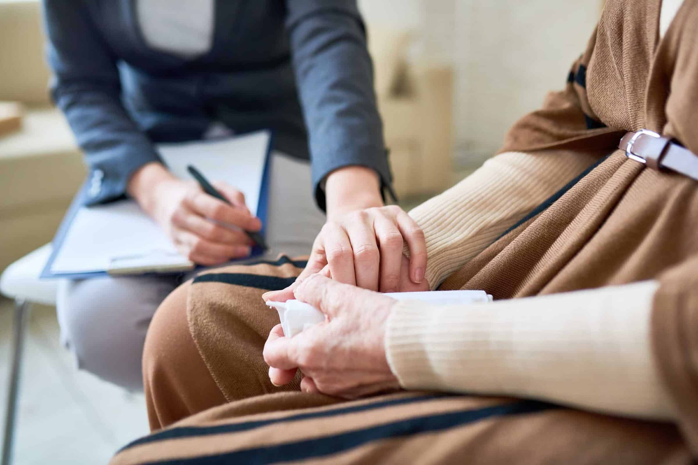 Close up of female psychologist holding hand of senior woman during therapy session